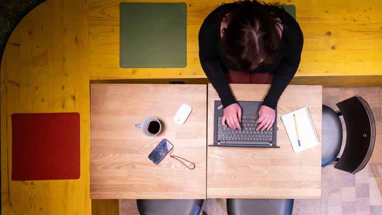 Eine Frau sitzt im Homeoffice am Küchentisch und arbeitet an einem Laptop (gestellte Szene).