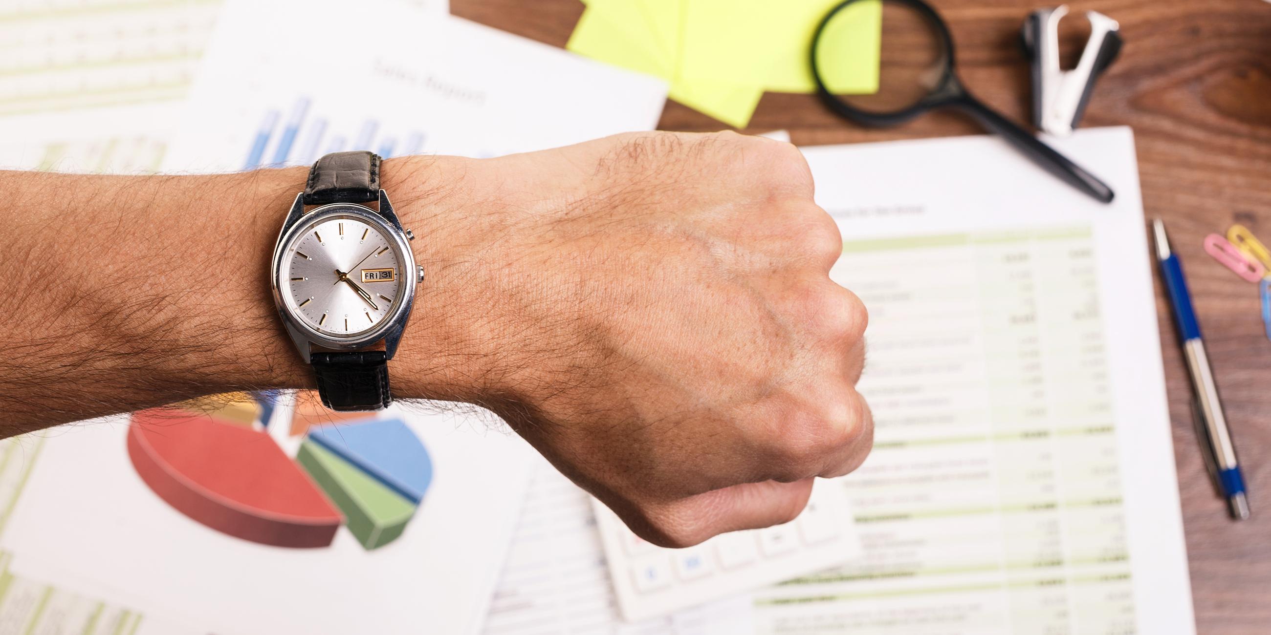 Mann schaut am Schreibtisch auf seine Armbanduhr