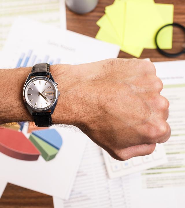 Mann schaut am Schreibtisch auf seine Armbanduhr