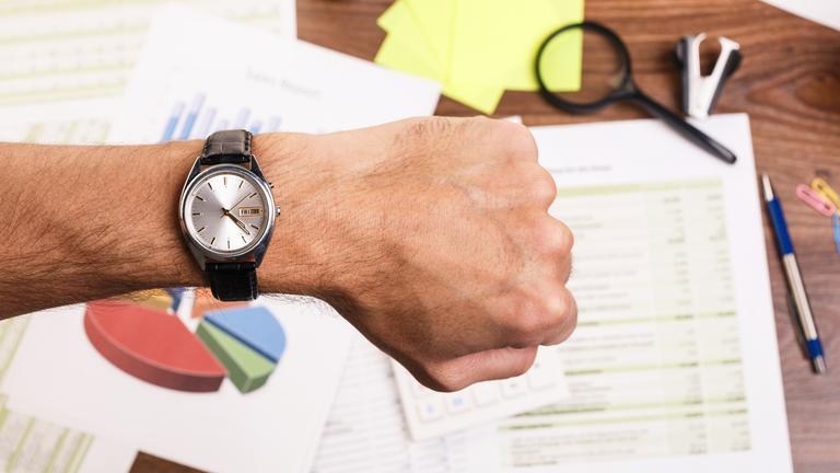 Mann schaut am Schreibtisch auf seine Armbanduhr