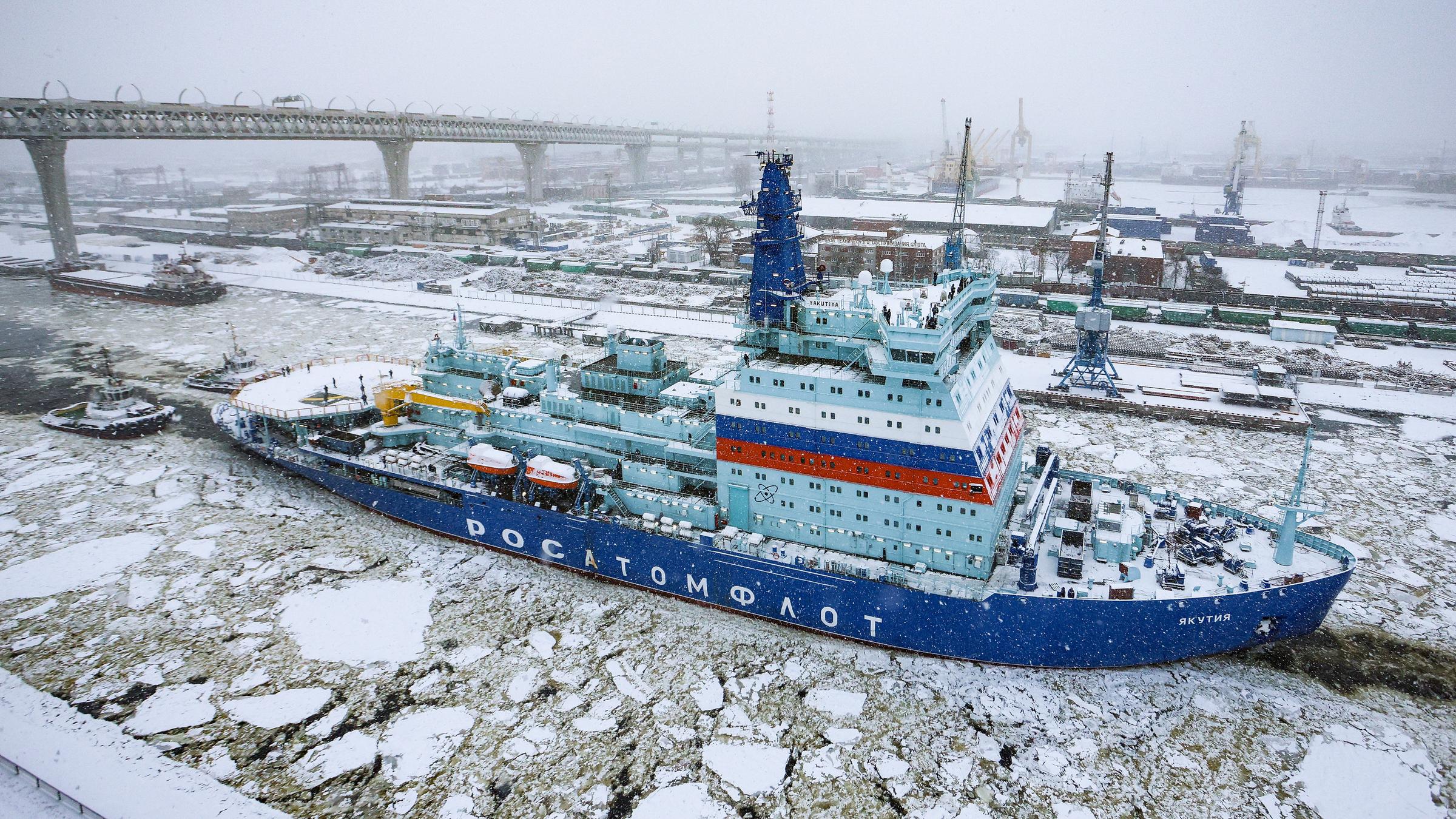 Ein blauer Eisbrecher fährt auf einem Fluss, auf dem Eisschollen schwimmen.