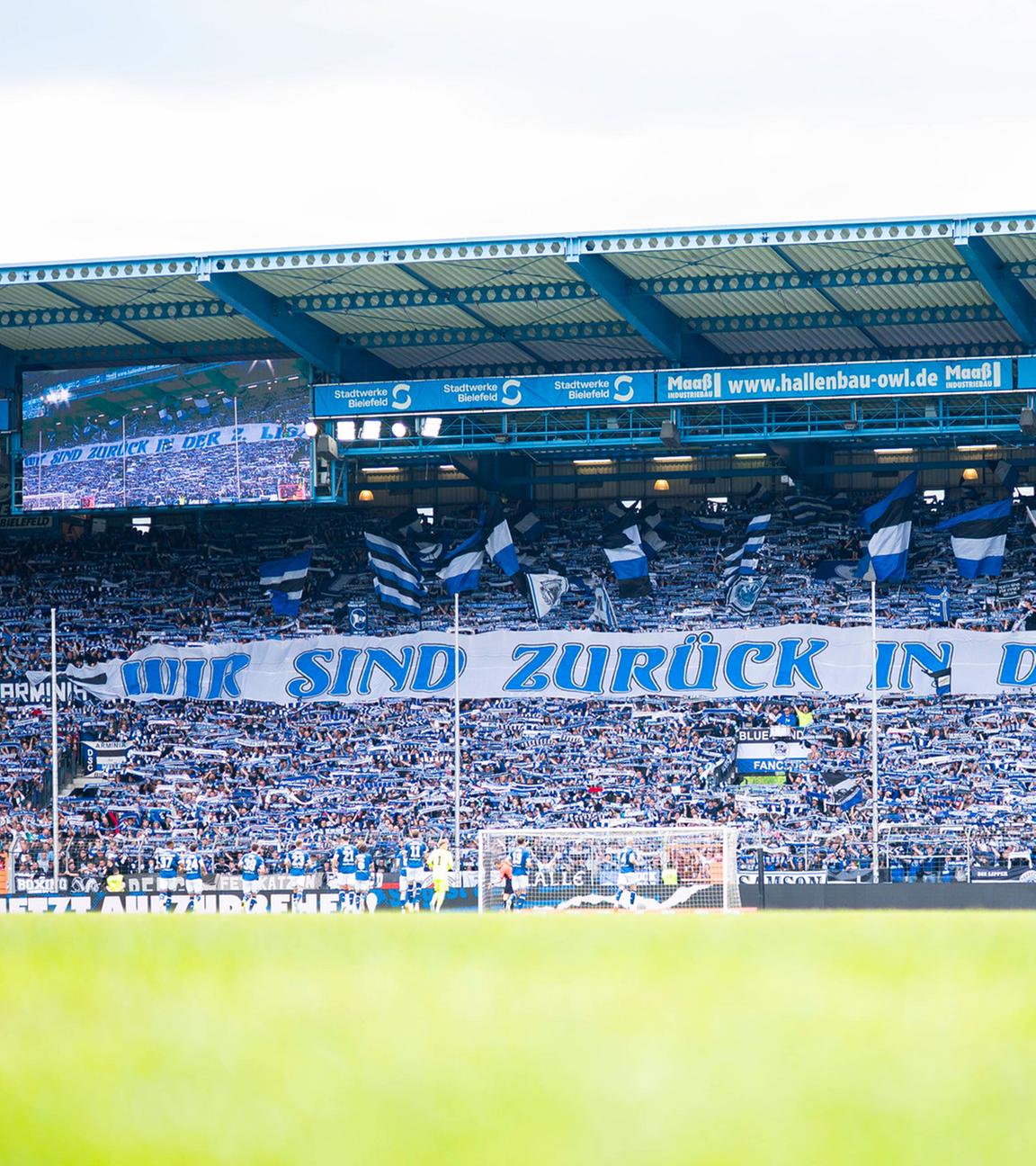 Fans von Arminia Bielefeld halten ein Banner mit der Aufschrift "Wir sind zurück in der 2. Liga. 