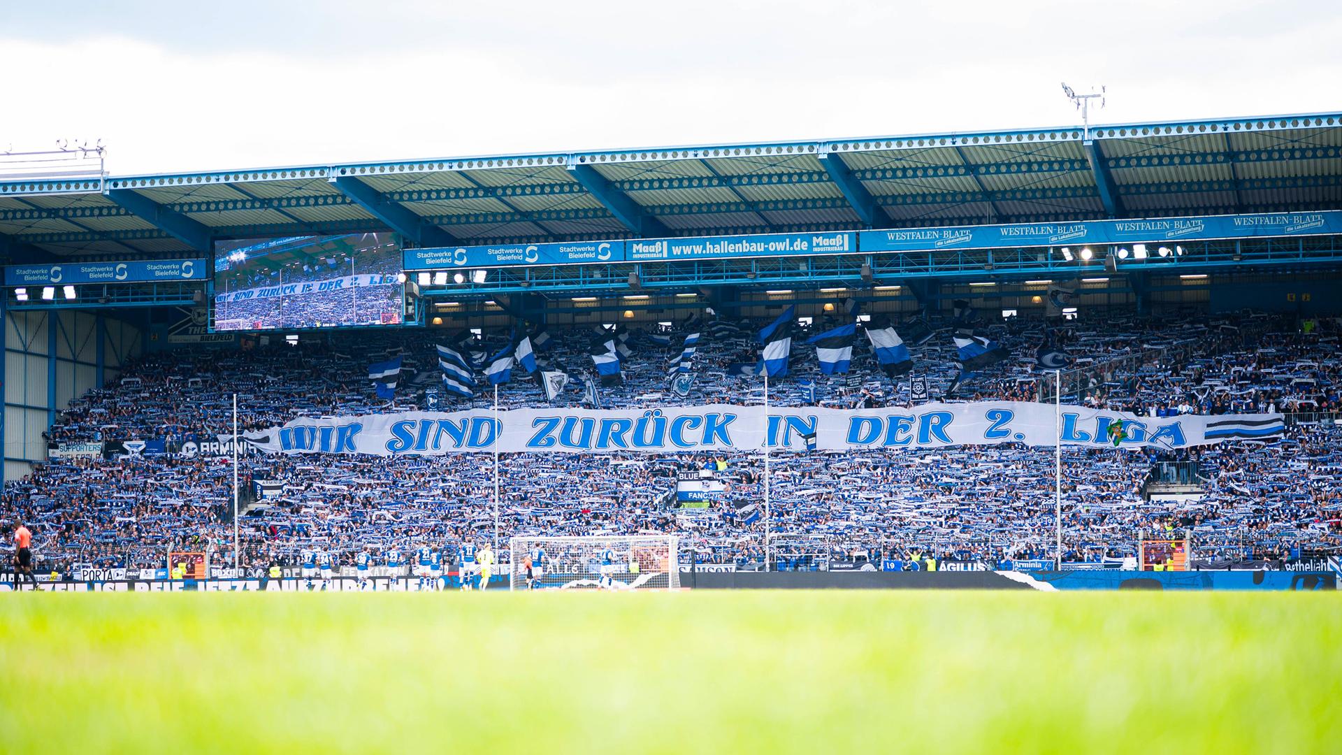 Fans von Arminia Bielefeld halten ein Banner mit der Aufschrift "Wir sind zurück in der 2. Liga. 