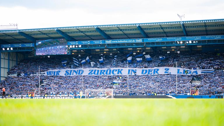 Fans von Arminia Bielefeld halten ein Banner mit der Aufschrift "Wir sind zurück in der 2. Liga. 