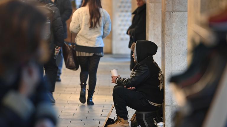 Ein junger Mann sitzt auf der Straße und bettelt.