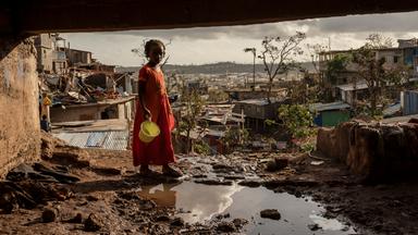 Ein junges Mädchen hält einen Eimer und steht in einem Slum in Mayotte.