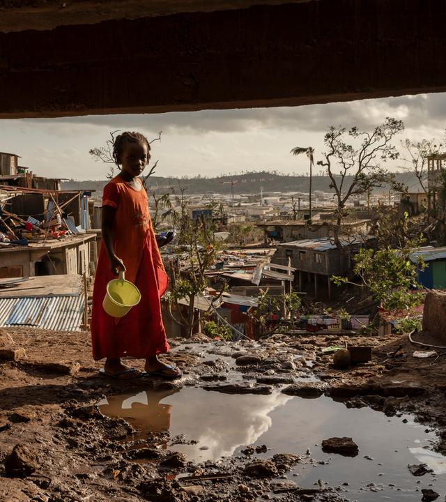 Ein junges Mädchen hält einen Eimer und steht in einem Slum in Mayotte.