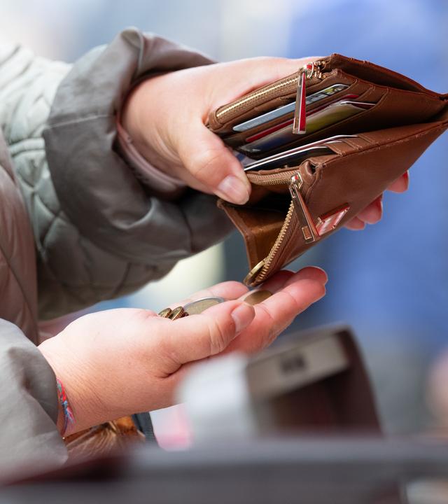 Ein Frau hält auf einem Wochenmarkt ein geöffnetes Portemonnaie. 