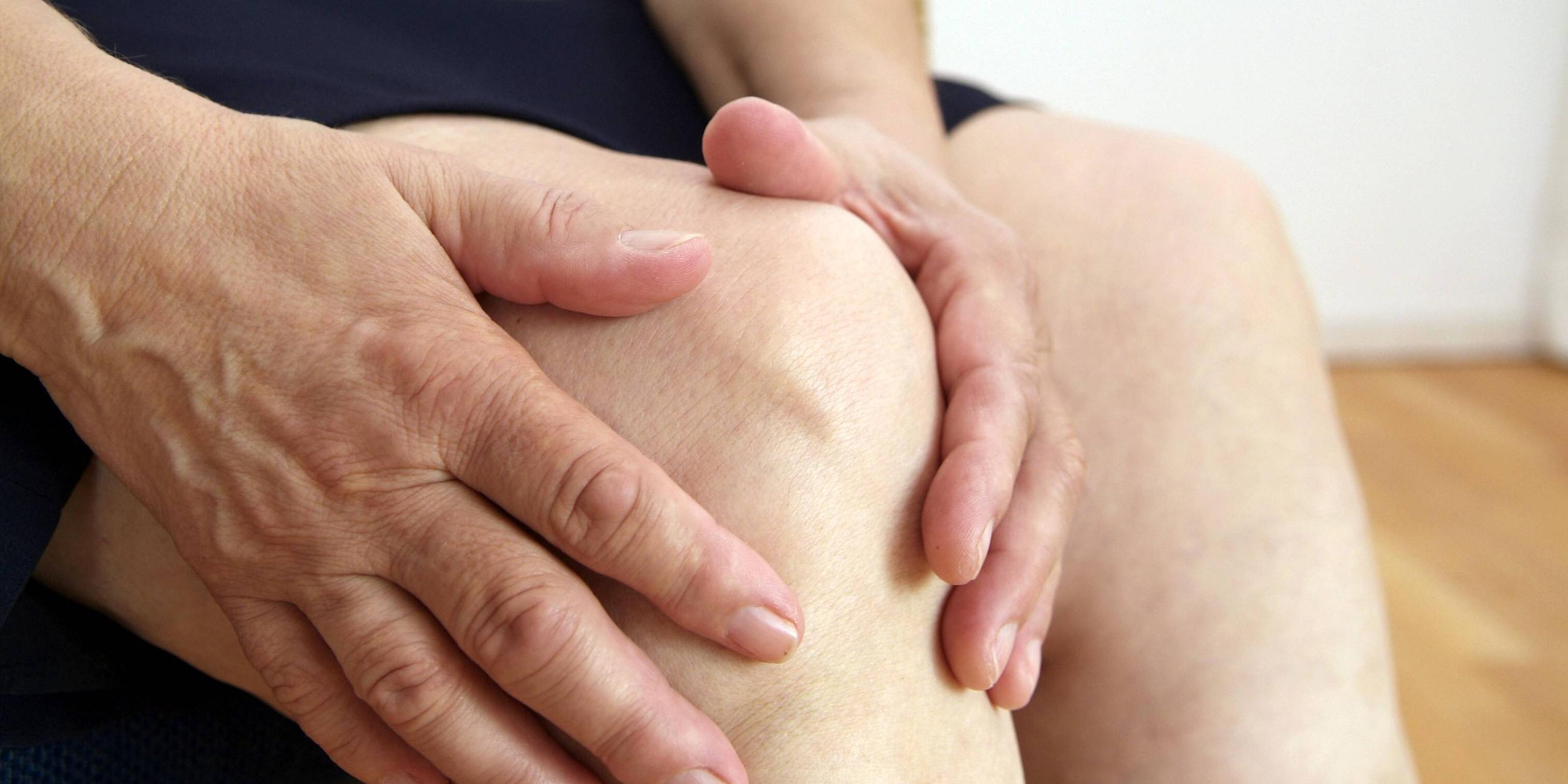 Eine Frau, die auf einem Stuhl sitzt, hält sich das Knie