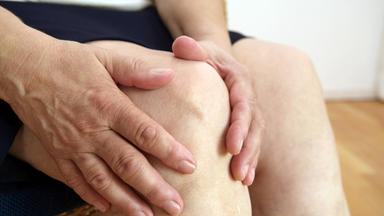 Eine Frau, die auf einem Stuhl sitzt, hält sich das Knie
