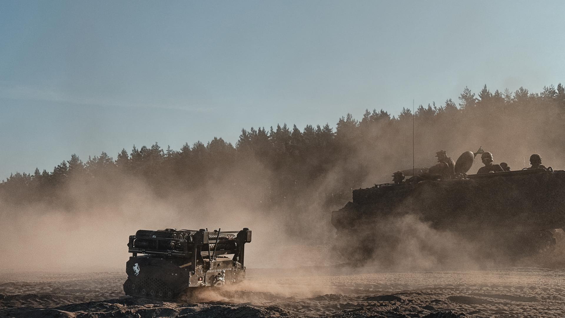 Ein Mini-Panzer steht auf einem Feld vor einem Truppentransporter.