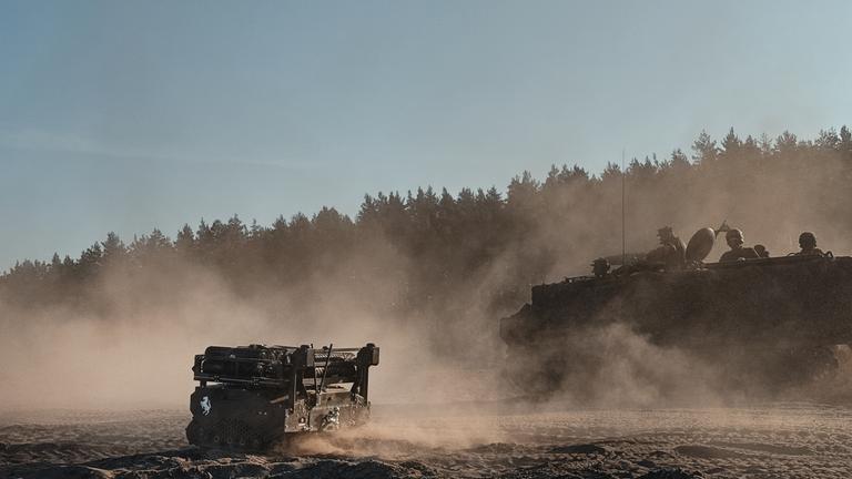 Ein Mini-Panzer steht auf einem Feld vor einem Truppentransporter.