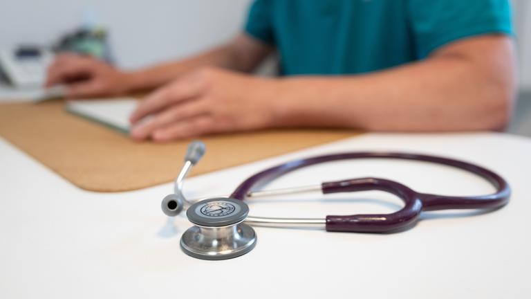 Sachsen, Dresden: Ein Hausarzt sitzt in einem Sprechzimmer seiner Hausarztpraxis an einem Schreibtisch neben einem Stethoskop und arbeitet am Computer.