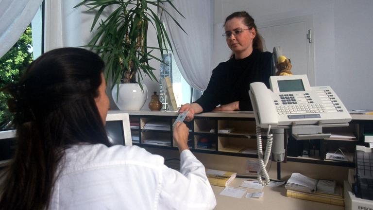 Eine Patientin meldet sich bei der Ankunft in einer Arztpraxis am Empfang
