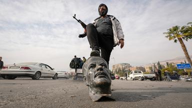 Rebellenkämpfer stellt Fuß auf Kopf einer gestürzten Statue von Bashar al-Assad