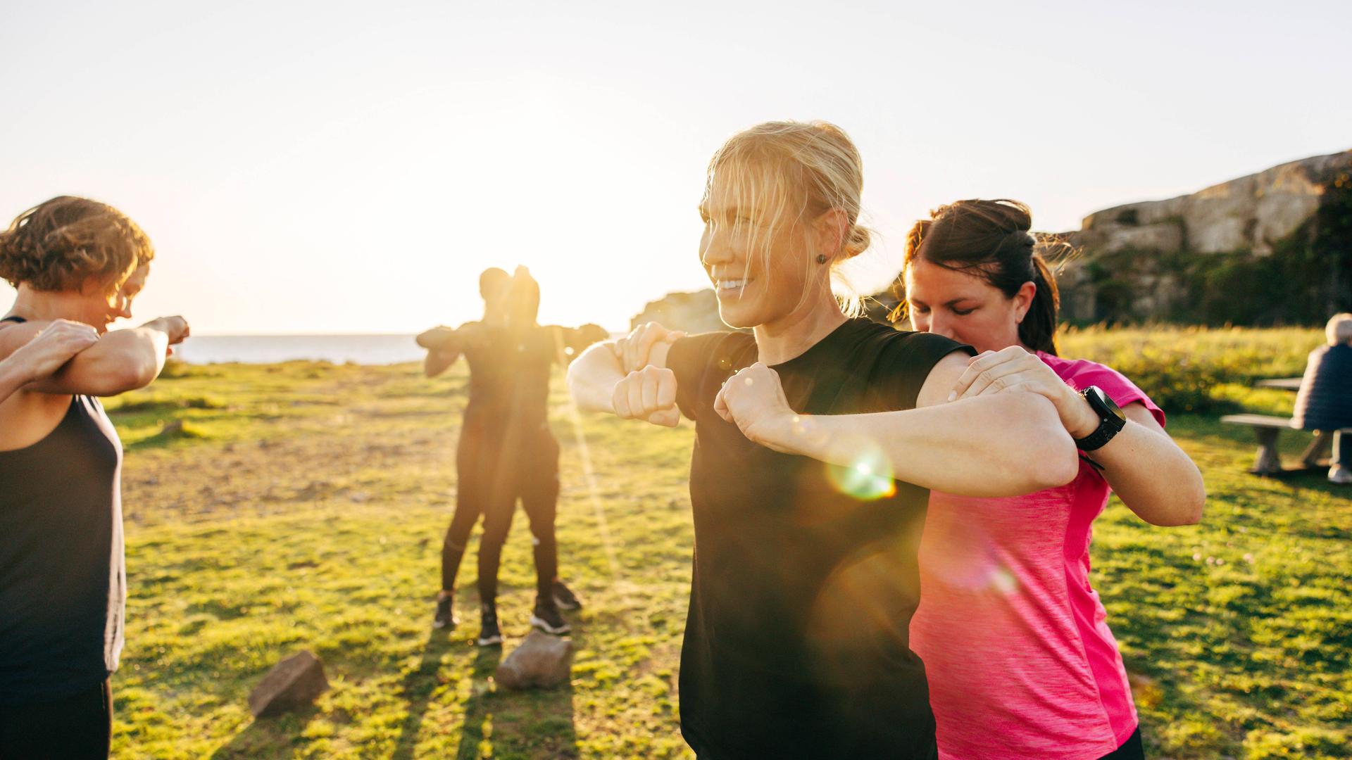 Trainerin unterstützt eine Frau bei Dehnungsübungen im Freien.