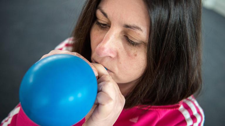 Eine Frau bläst einen blauen Ballon auf.