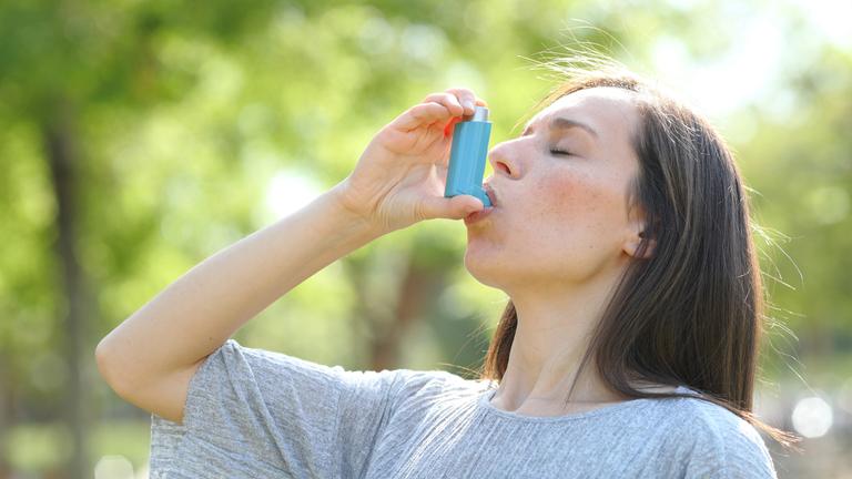 Frau in der Natur inhaliert Asthma-Spray ein.