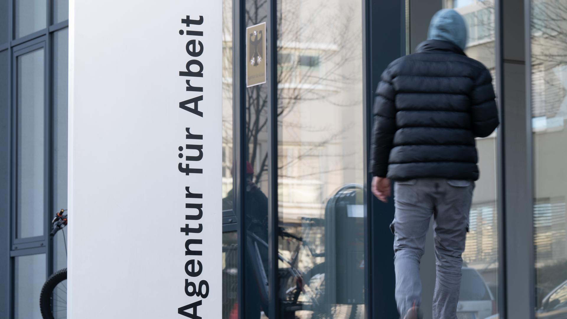 Ein Mann läuft neben einem Schild für die Agentur für Arbeit