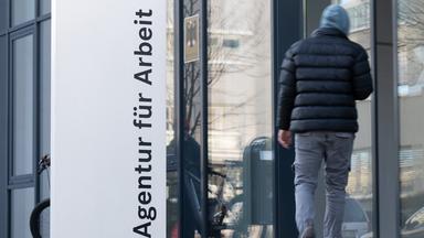 Ein Mann läuft neben einem Schild für die Agentur für Arbeit