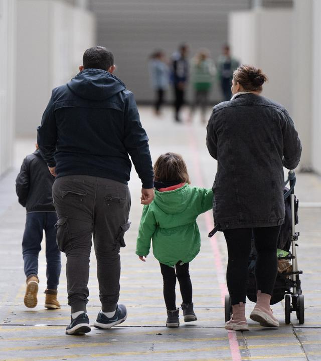 Eine Flüchtlingsfamilie geht durch die zu einer Massenunterkunft umfunktionierten Messehalle in Frankfurt. (Archivbild) 
