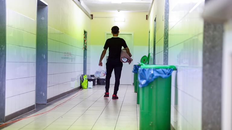 Ein Migrant geht in der Zentralen Aufnahmeeinrichtung für Asylbewerber in Bayern mit der Erstausstattung an Besteck, Bettwäsche und Hygieneartikeln über einem Gang zu seinem Wohnbereich.