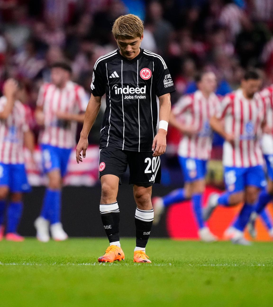 Atletico Madrid - Eintracht Frankfurt: Ritsu Doan steht bedrückt auf dem Platz, während im Hintergrund Atletico-Spieler jubeln.