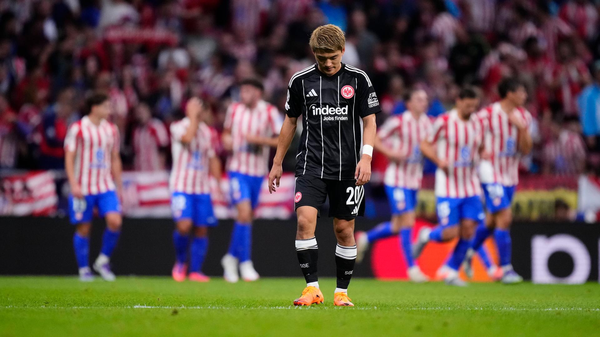 Atletico Madrid - Eintracht Frankfurt: Ritsu Doan steht bedrückt auf dem Platz, während im Hintergrund Atletico-Spieler jubeln.