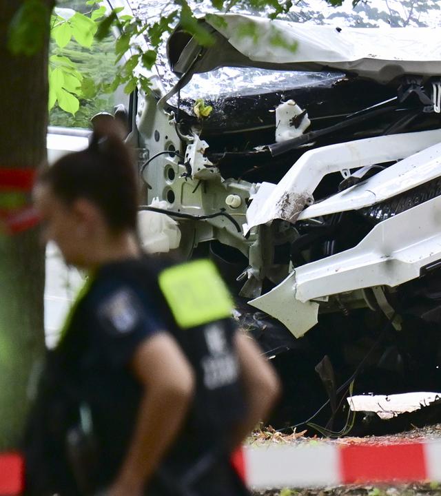 Eine Polizeibeamtin läuft zwischen Bäumen im Bereich des Tiergartens an einem zerstörten weißen Fahrzeug vorbei, das einen Baum gerammt hatte.
