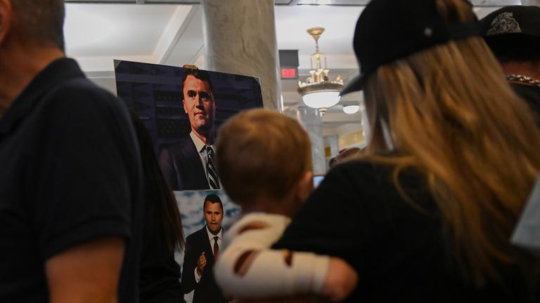  Ein Foto des getöteten rechtskonservativen Podcasters Charlie Kirk steht im Utah State Capitol, davor steht eine Frau mit einem Baby auf dem Arm.