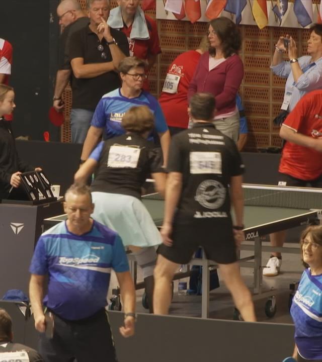 Halle mit Menschen in Sportkleidung und Tischtennisplatten