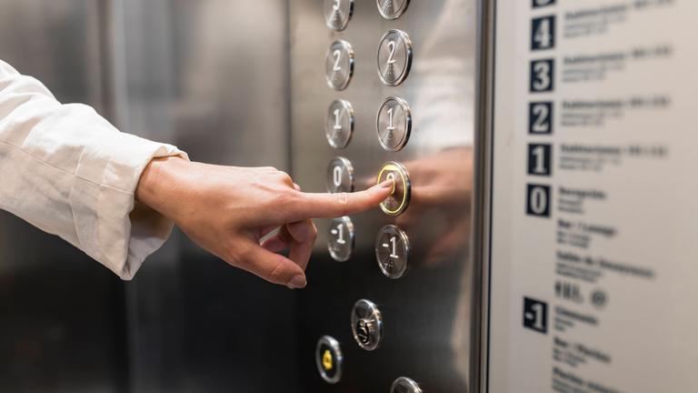 Symbolbild: Frau drückt Knopf in einem Fahrstuhl
