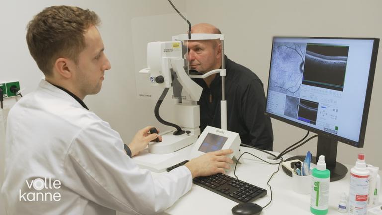Mann und Arzt sitzen sich gegenüber; Mann schaut mit einem Auge in ein medizinisches Gerät