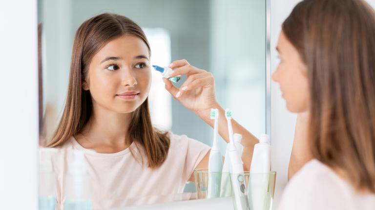 Ein Mädchen steht in einem Badezimmer vor dem Spiegel und verwendet Augentropfen.