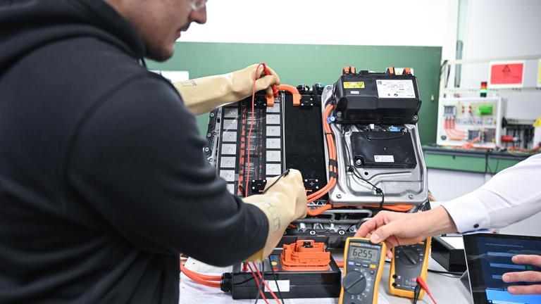 Symbolbild: Berufsschüler lernen im praktischen Unterricht in einem Schulraum mit einem Kfz-Labor Kfz-Hochvolttechnik. 
