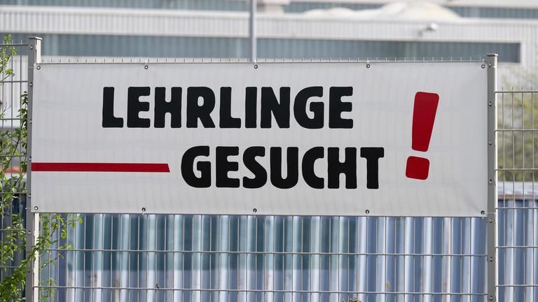 Ein Banner mit der Aufschrift Lehrlinge gesucht hängt an einem Zaun.