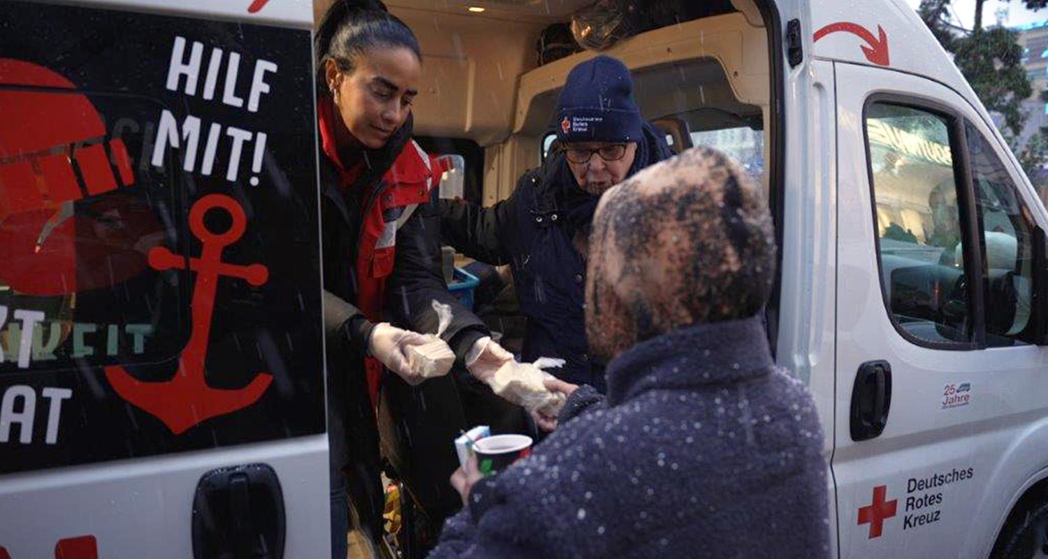 Zwei Helferinnen reichen Brötchen aus dem Wagen an eine Person.