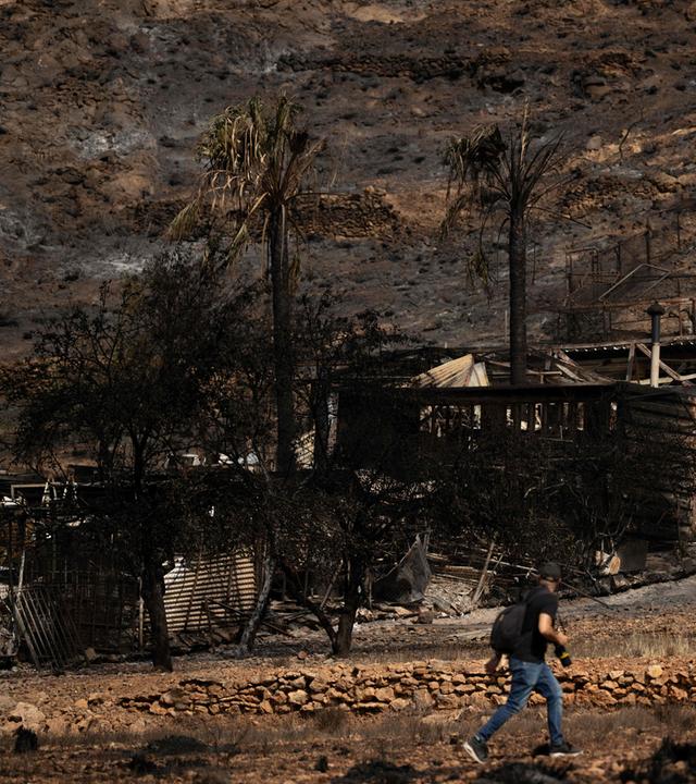 Ein Mann geht am 11.07.2026 in Bedar, bei Almería, an einem ausgebrannten Haus vorbei, nachdem ein Waldbrand mindestens 12 Menschen das Leben gekostet hatte. 