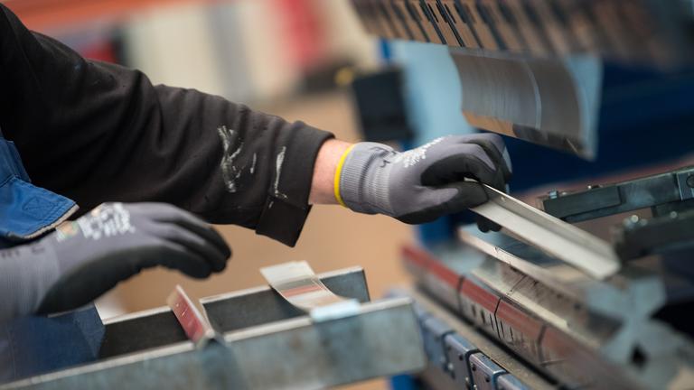 Bandenburg, Esterwerda: Ein Mitarbeiter bedient in der Produktionshalle einer Firma eine Metallpresse. 
