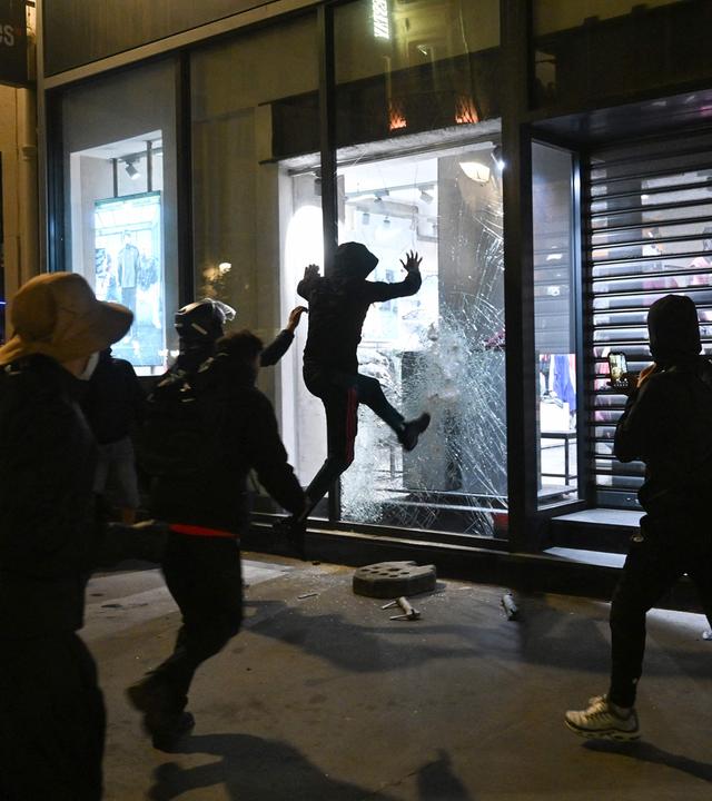 Vermummte Personen brechen in einen Laden in Paris ein. 