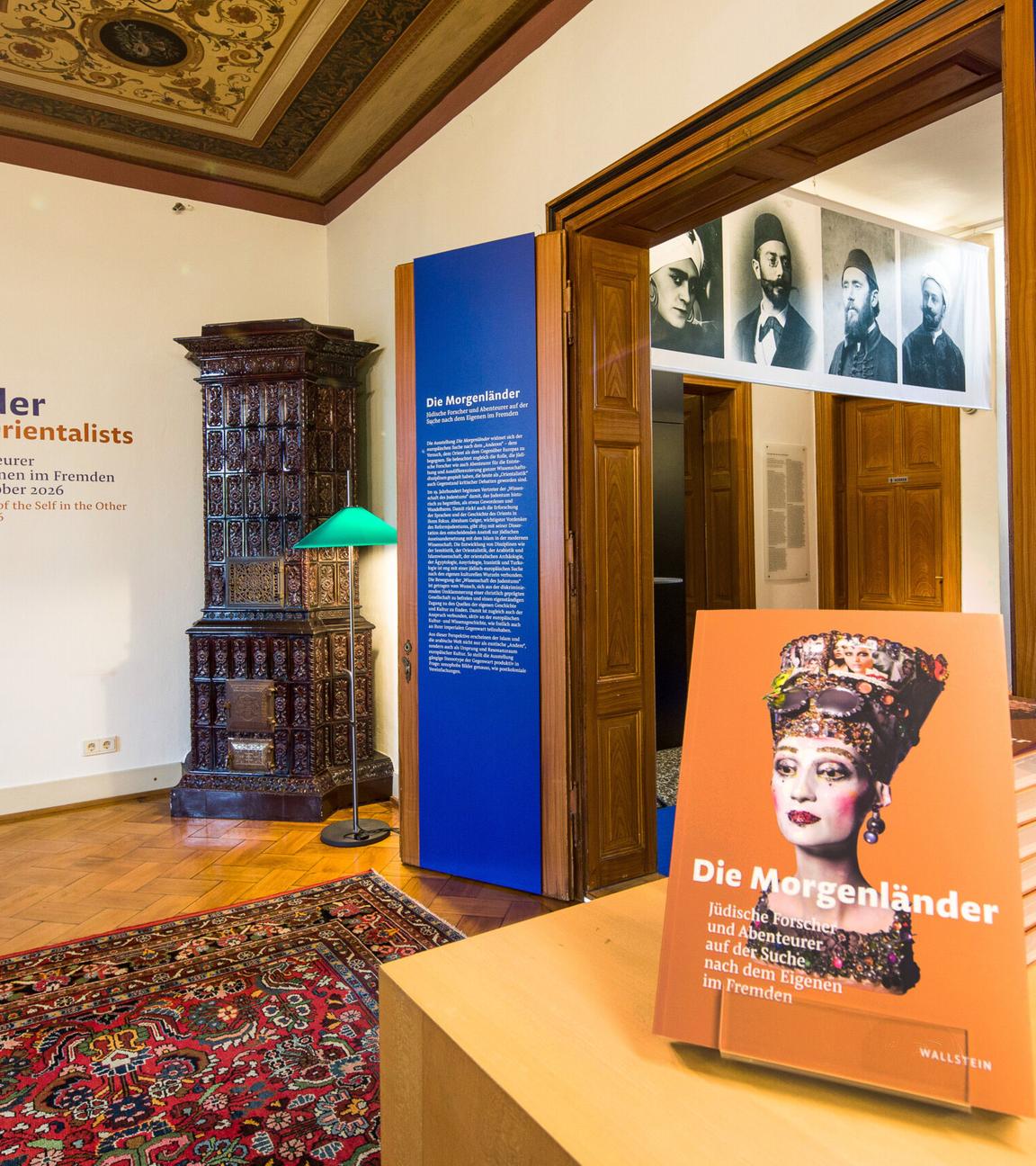 In einem Ausstellungsraum stehen Exponate und hängen Bilder von Personen an der Wand.