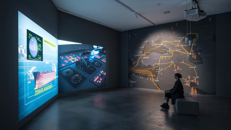 In einem Ausstellungsraum schaut sich eine Frau eine Videoinstallation an.