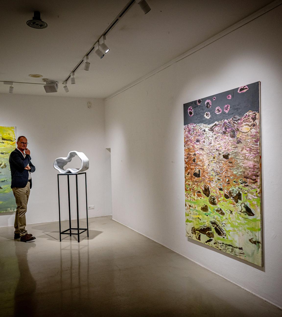 Ein Mann sieht sich eine moderne Skulptur in einem Ausstellungsraum an. An den Wänden hängen abstrakte Gemälde.