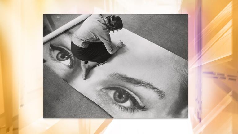 Man sieht eine Schwarz-Weiß-Fotografie, auf der eine Frau am Boden sitzt und an einem Kunstwerk arbeitet.