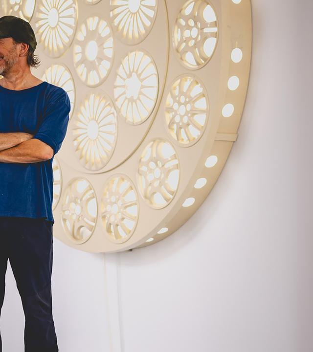 Ein Mann mit Baseballkappe steht vor einem weißen, modernen Kunstwerk, welches an einer Wand hängt.