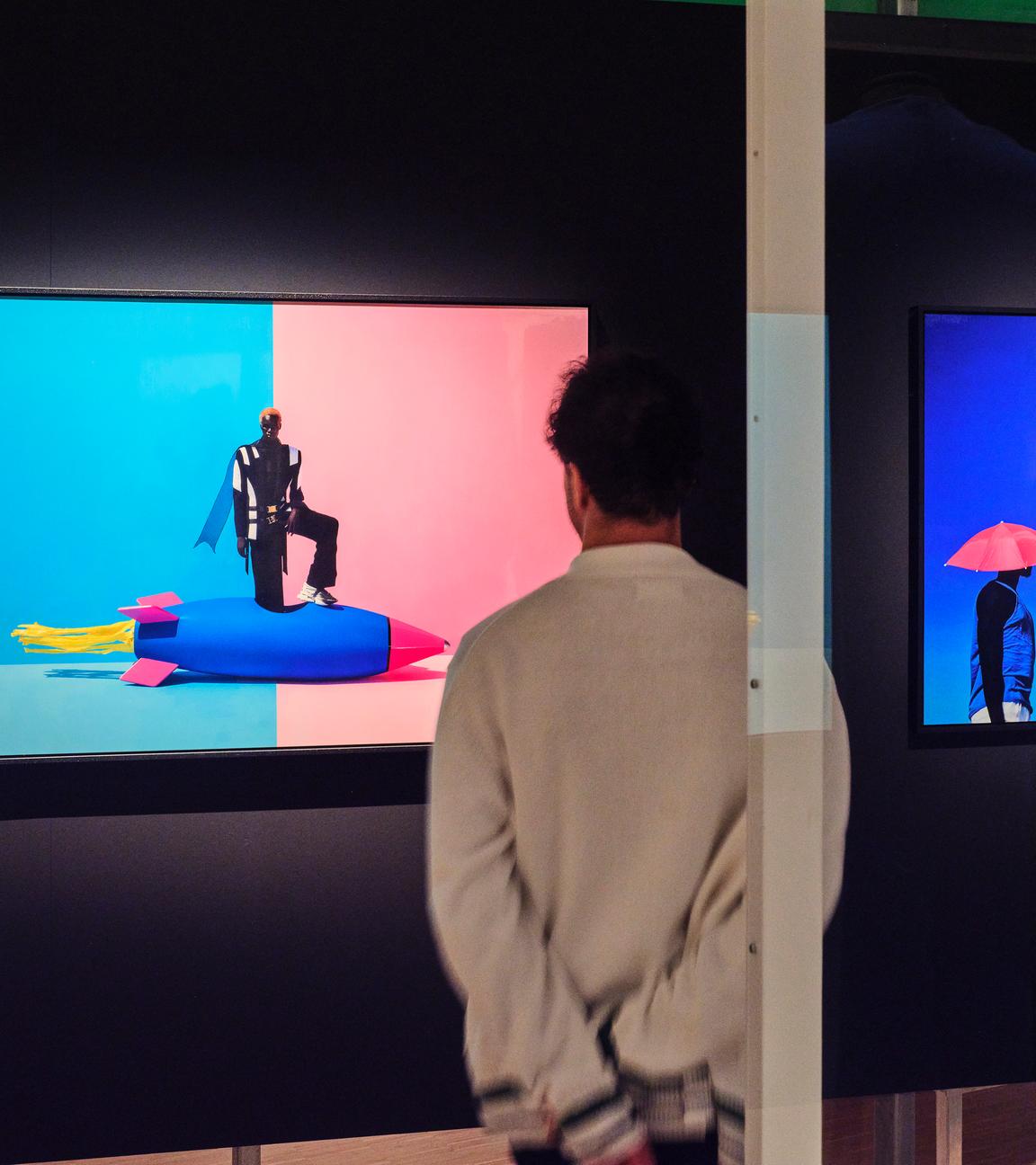 In einem abgedunkelten Ausstellungsraum schaut ein Mann sich ein modernes, buntes Bild an, auf dem eine Person auf einer bunten Rakete steht.