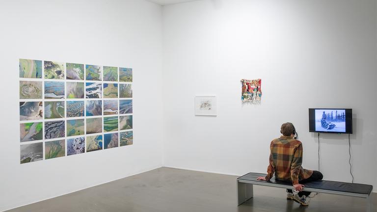 In einem Ausstellungsraum sitzt ein Mann der sich die Exponate ansieht. 