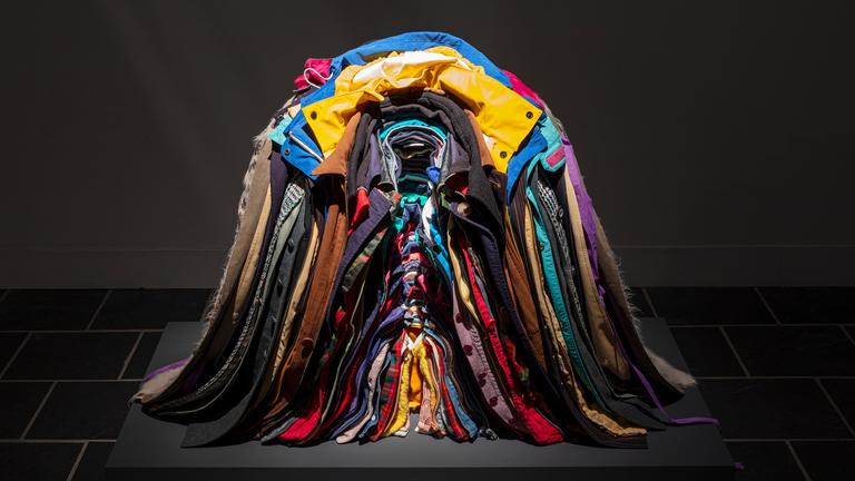 Zu sehen ist ein bunter, ordentlich ineinander gestapelter Haufen aus Jacken.