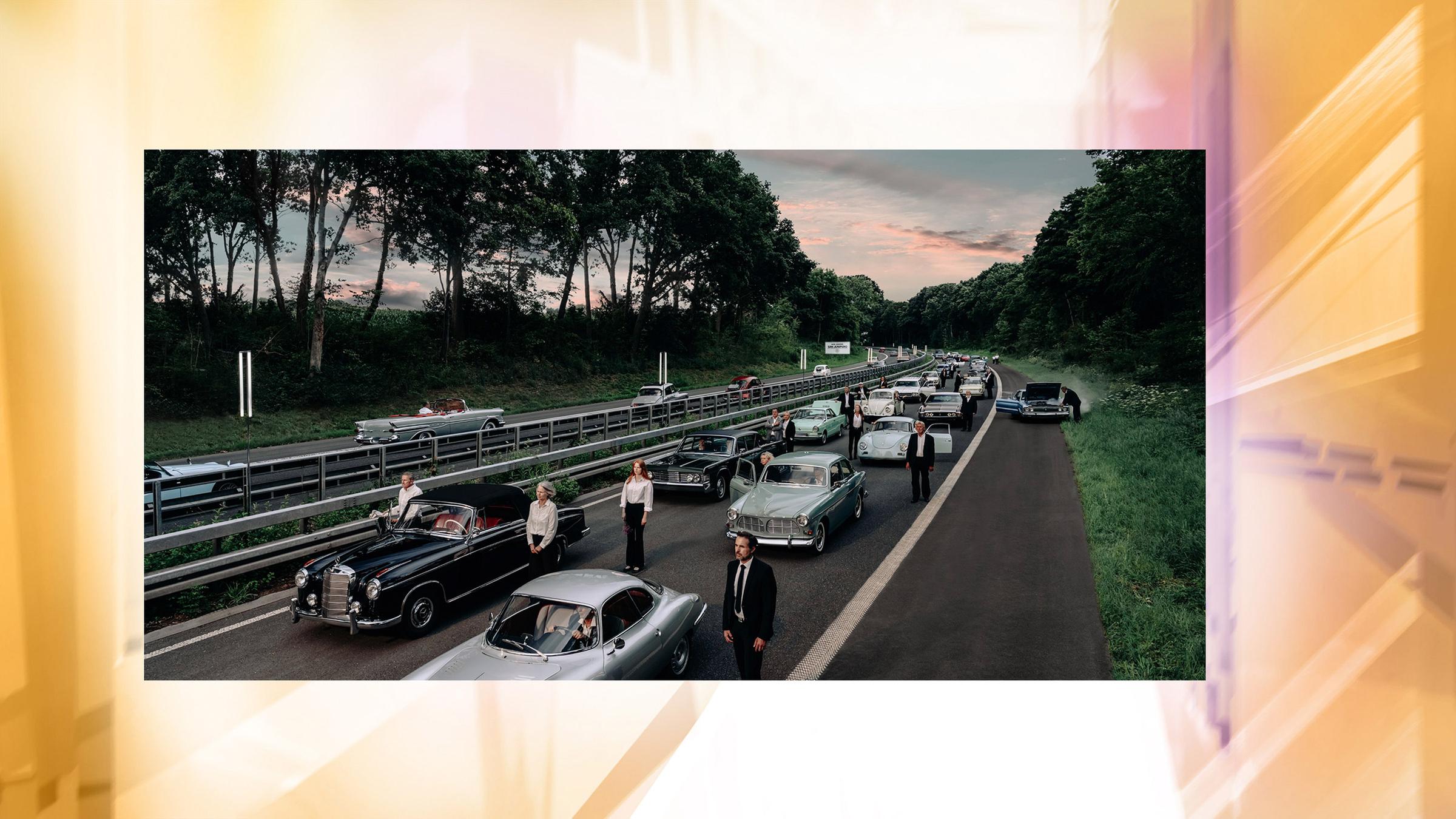 Auf einer Aotobahn stehen Autos im Stau und Menschen drumherum. Sie schauen alle in eine Richtung.