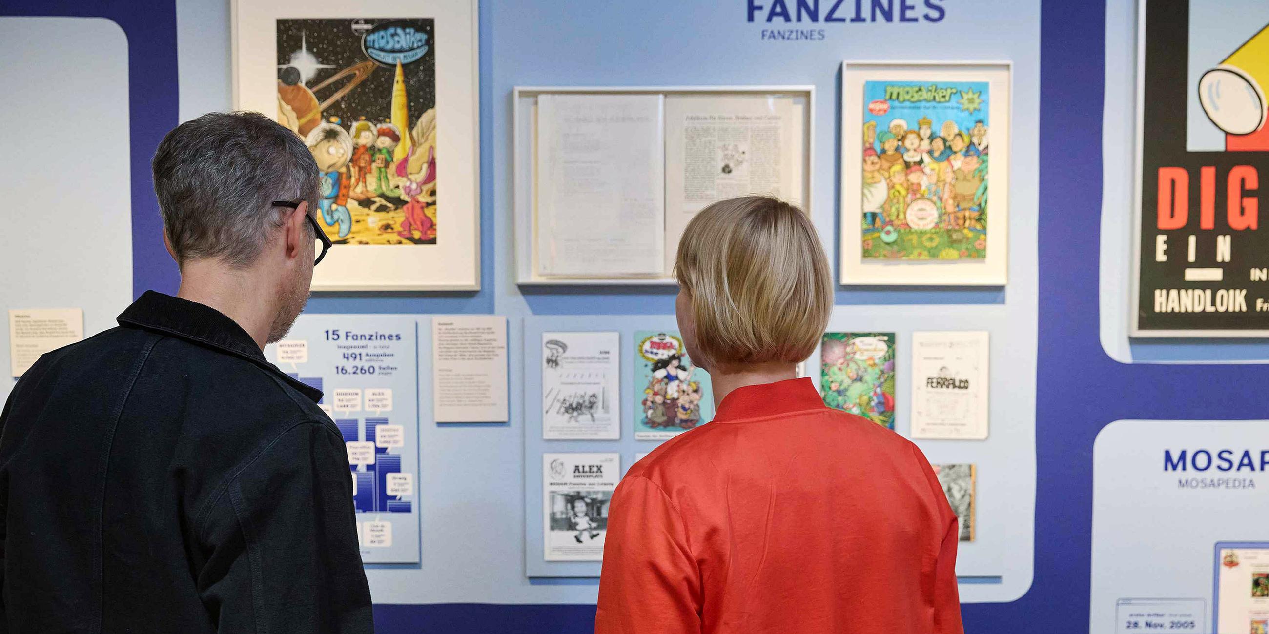 In einem Austellungsraum schauen sich ein Mann und eine Frau Comic-Exponate an.